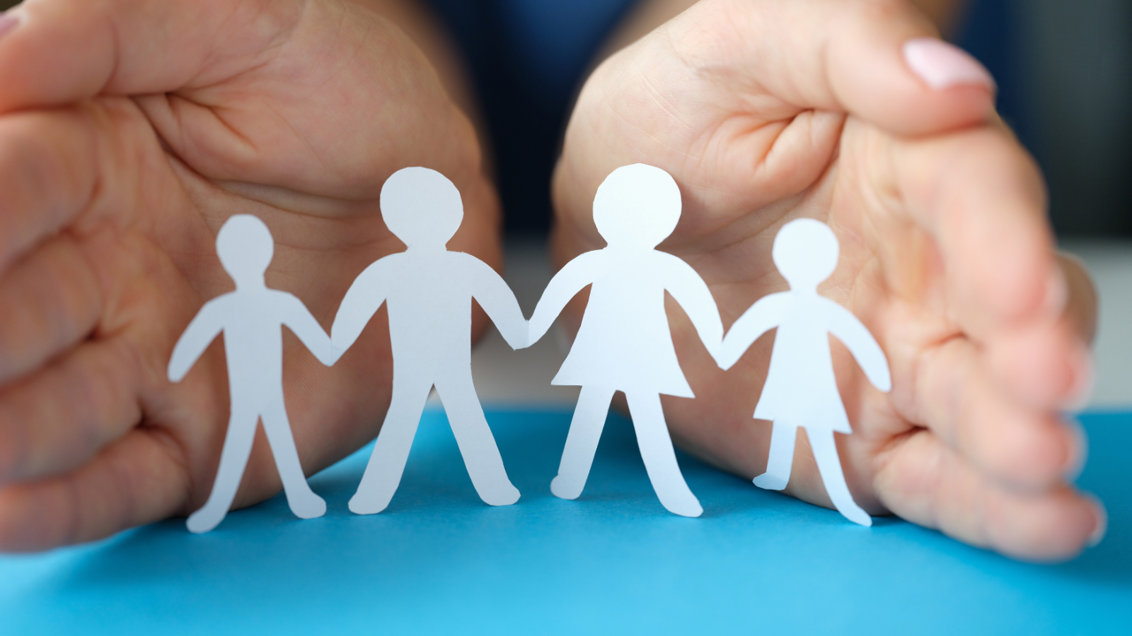 Paper cut-outs of children holding hands, in front of two real human hands